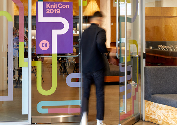 A male walking into Pinterest Headquarters, the glass door has signage for KnitCon 2019